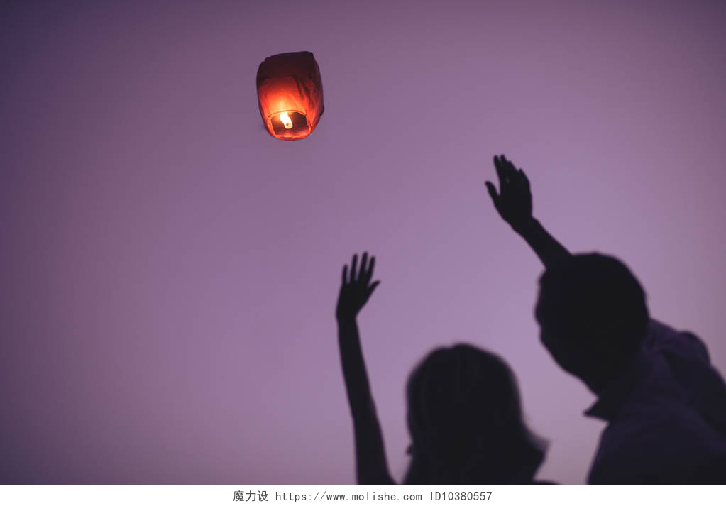 把孔明灯放上天空的夫妻晚上的一对夫妇挥舞着手的剪影空中灯笼